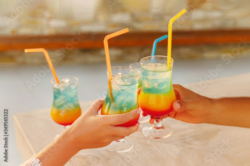 Glasses of rainbow cocktails in hands at sunset. Summer holidays. 
