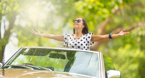 Canvas-taulu Woman in sunglasses sits on top of the convertible, arms wide open, soaking up t