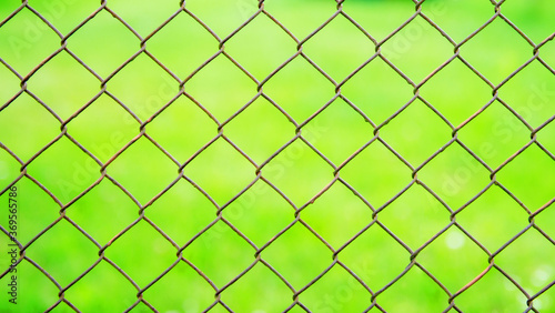A wire mesh cage against a green meadow. Texture pattern surface background from wire mesh netting. Out of focus, defocus.