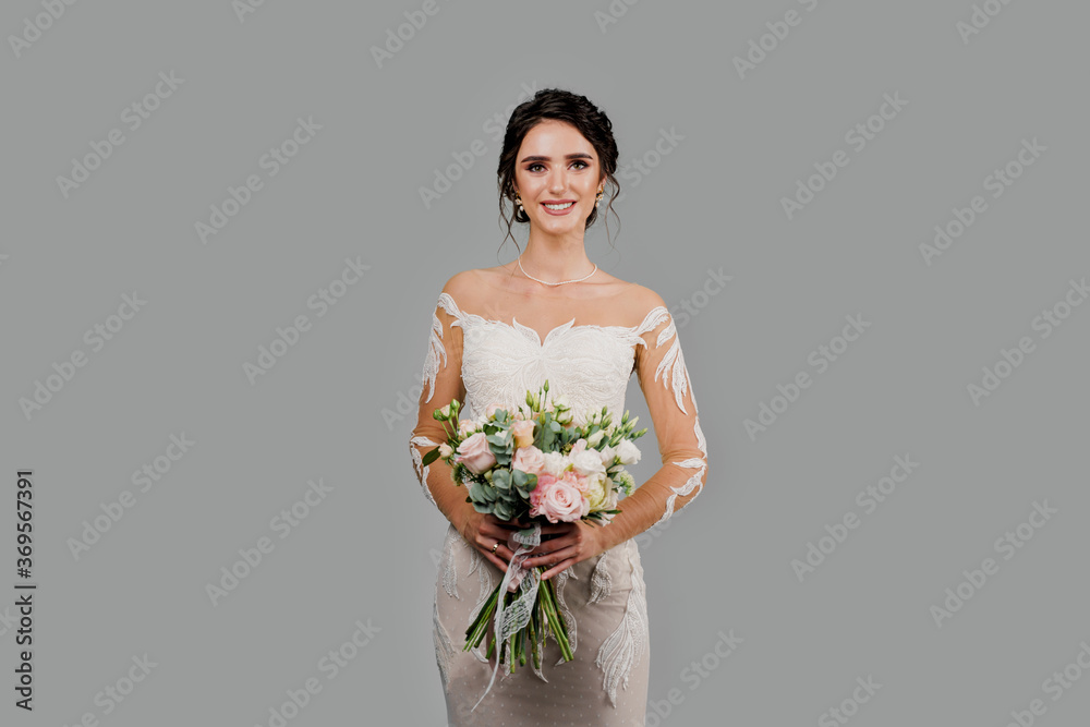 Bride with wedding bouquet smiles, looks in camera and touches her face. Attractive girl portrait for social networks. Girl in wedding gown on blank background Bride with wedding bouquet smiles, looks in camera and touches her face. Attractive girl portrait for social networks. Girl in wedding gown on blank background