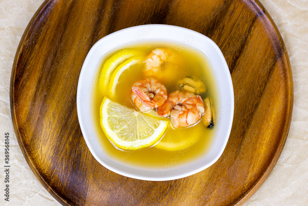 Top view of white bowl with traditional light spicy thai cuisine tom yam soup with shrimps, seafood and lemon on wooden board background. Top view of white bowl with traditional light spicy thai cuisine tom yam soup with shrimps, seafood and lemon on wooden board background.