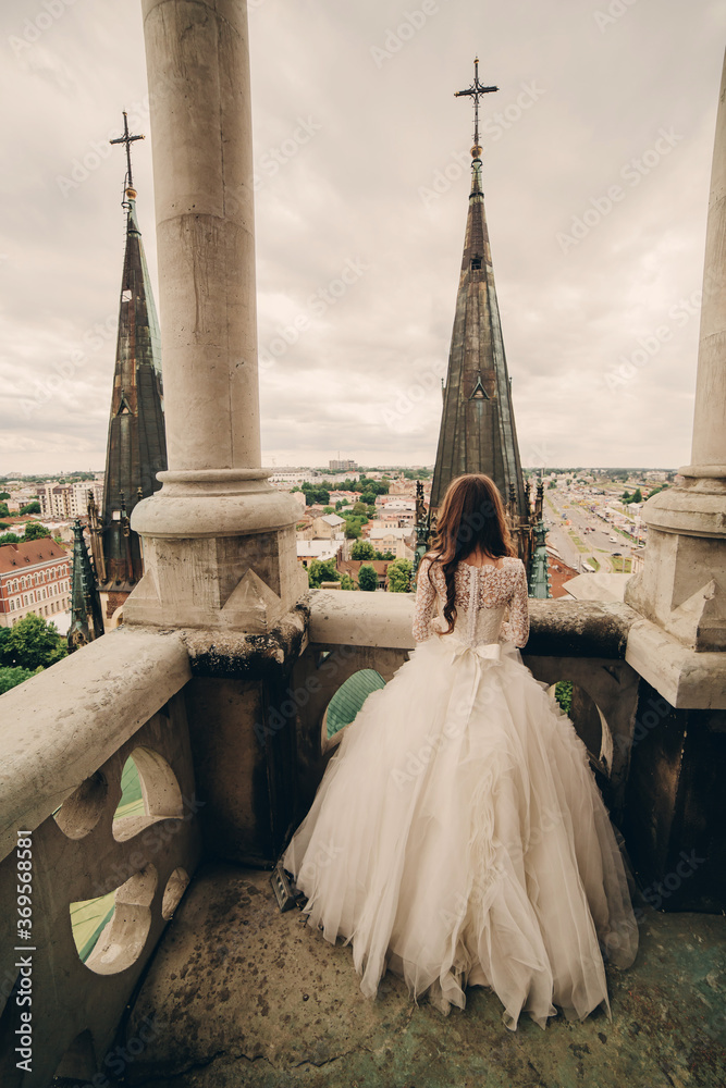 Happy newlywed. beautiful bride in long luxury white dress on the balcony of old gothic cathedral with panoramic city views