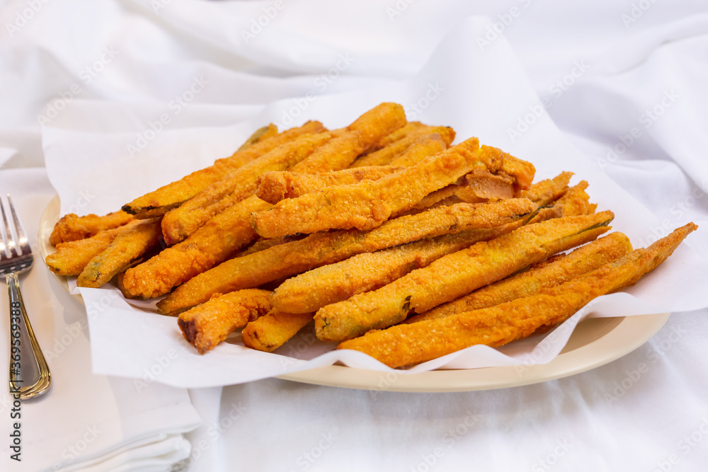 A view of a plate of deep fried zucchini fries, in a restaurant or kitchen setting. A view of a plate of deep fried zucchini fries, in a restaurant or kitchen setting.