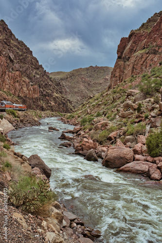 Arkansas river in Royal Gorge with train running parallel. Sky visible in ravine on cloudy day.