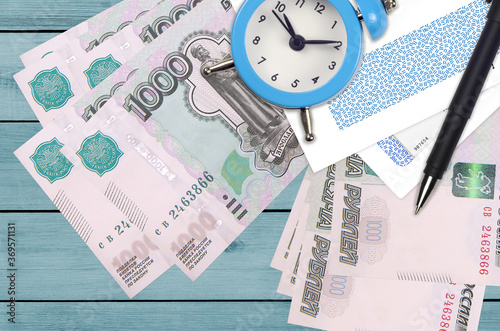 1000 russian rubles bills and alarm clock with pen and envelopes. Tax season concept, payment deadline for credit or loan. Financial operations using postal service photo