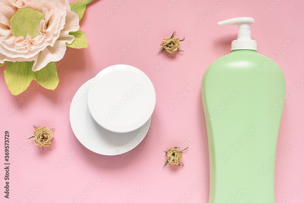 Flat lay composition with natural cosmetic products on pink background. Top view face and body cream in jar, shower gel and three dry roses. Natural organic beauty product concept.