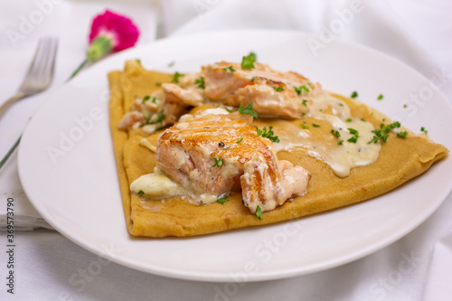 A view of a French crepe with salmon filet and cream sauce, in a restaurant or kitchen setting.