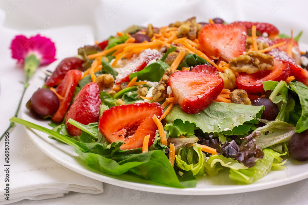 A view of a garden salad, featuring strawberry slices and walnut slivers, in a restaurant or kitchen setting.