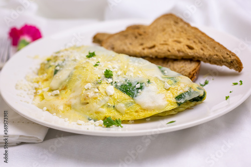 A view of a plate with a spinach omelet and slices of wheat bread toast, in a restaurant or kitchen setting.