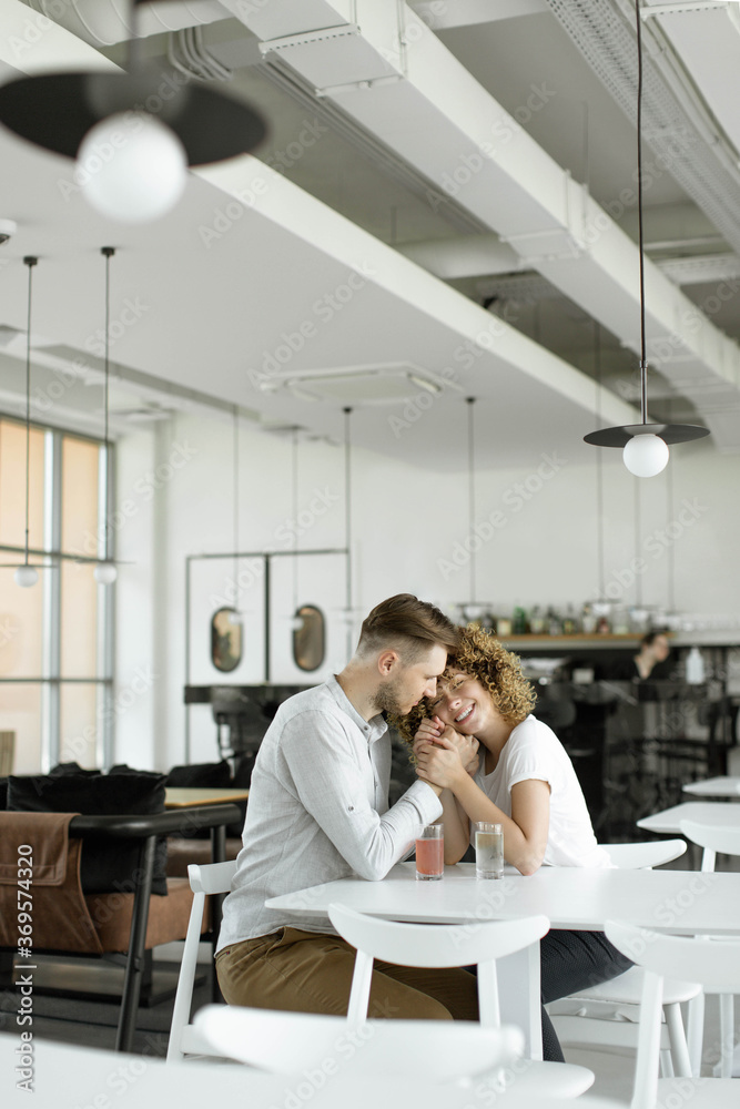 Happy couple, husband and wife are hugging in a cafe against a background of light walls. Happy couple, husband and wife are sitting in a cafe and drinking drinks. Close-up. Happy couple, husband and wife are hugging in a cafe against a background of light walls. Happy couple, husband and wife are sitting in a cafe and drinking drinks. Close-up.