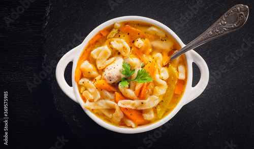  Russian homemade chicken soup with noodles and vegetables in a white plate on a black background