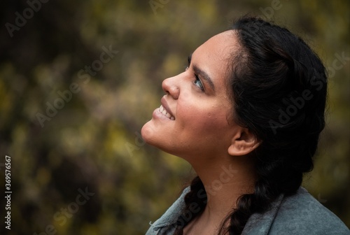Hispanic happy young woman looking around in the forest on a green and yellow background. White adult with black hair and black eyes 