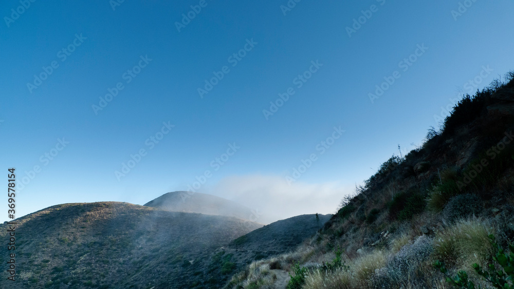 Looking east in the morning from Point Mugu State Park's trail, misty clouds cover distant mountains with fog.
