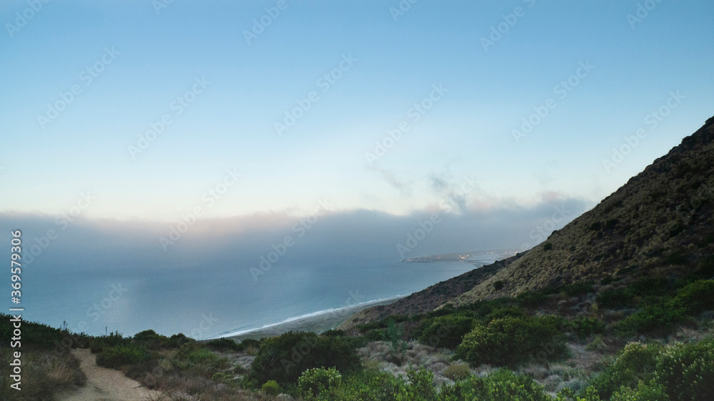 Point Mugu State Park, California. Pacific Coast visible at the bottom. Tall grasses and shrubs dot the desert mountain. Point Mugu Naval Air Station is visible in the distance. 