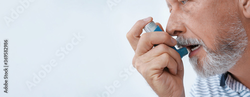 Closeup view of man using asthma inhaler on white background, space for text. Banner design