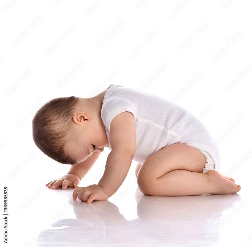 Portrait of sweet cute baby boy toddler in white body barefoot crawling on floor and looking down at legs