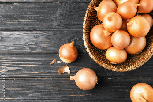 Ripe onion bulbs and basket on black wooden table, flat lay. Space for text