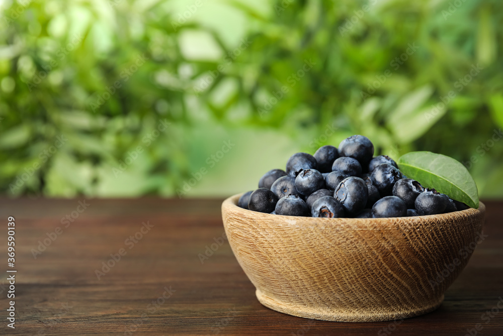 Tasty ripe blueberries in bowl on wooden table, space for text