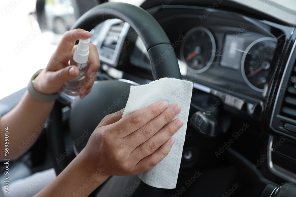 Woman cleaning steering wheel with wet wipe and antibacterial spray in car, closeup