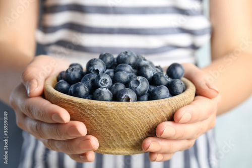 Woman holding fresh ripe blueberries in wooden bowl, closeup