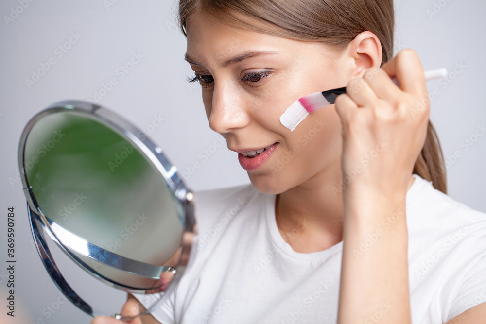 Young woman applying moisturizer on her face in front of mirror Young woman applying moisturizer on her face in front of mirror