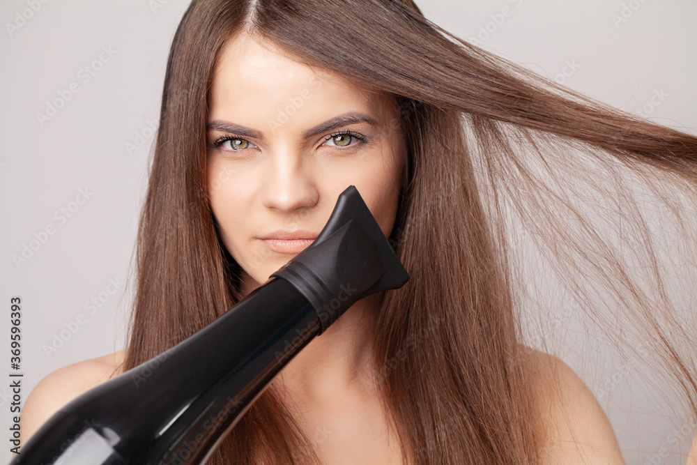 Fototapeta premium Beautiful smiling woman drying her long hair with dryer