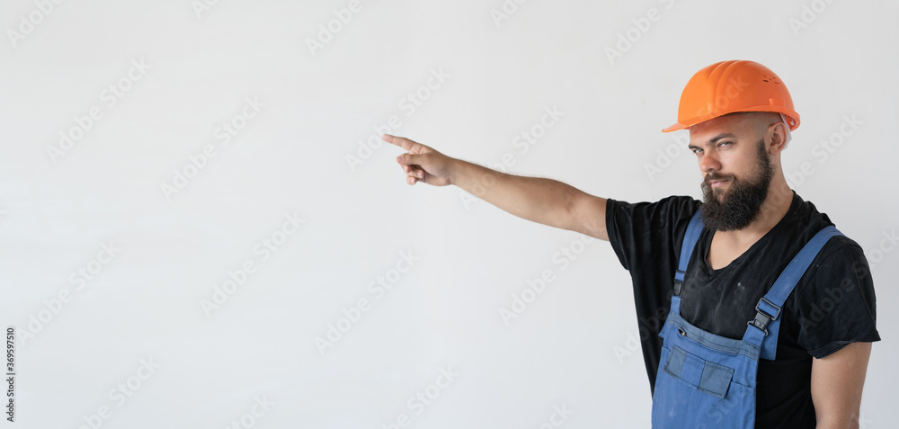 A builder in an orange helmet and uniform is standing in the room, pointing to an empty spot with his finger. A builder in an orange helmet and uniform is standing in the room, pointing to an empty spot with his finger.
