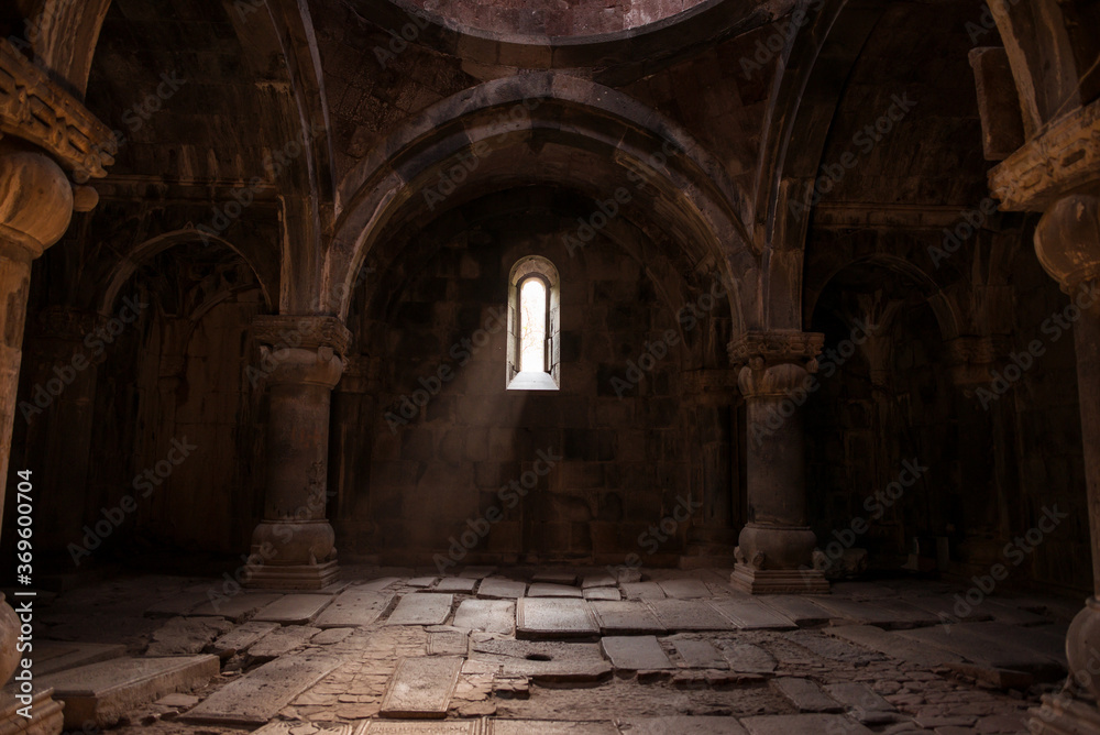 Interior of old Sanahin Armenian Monastery of the Armenian Apostolic Church with ray of light entering through narrow window and headstones on uneven ground