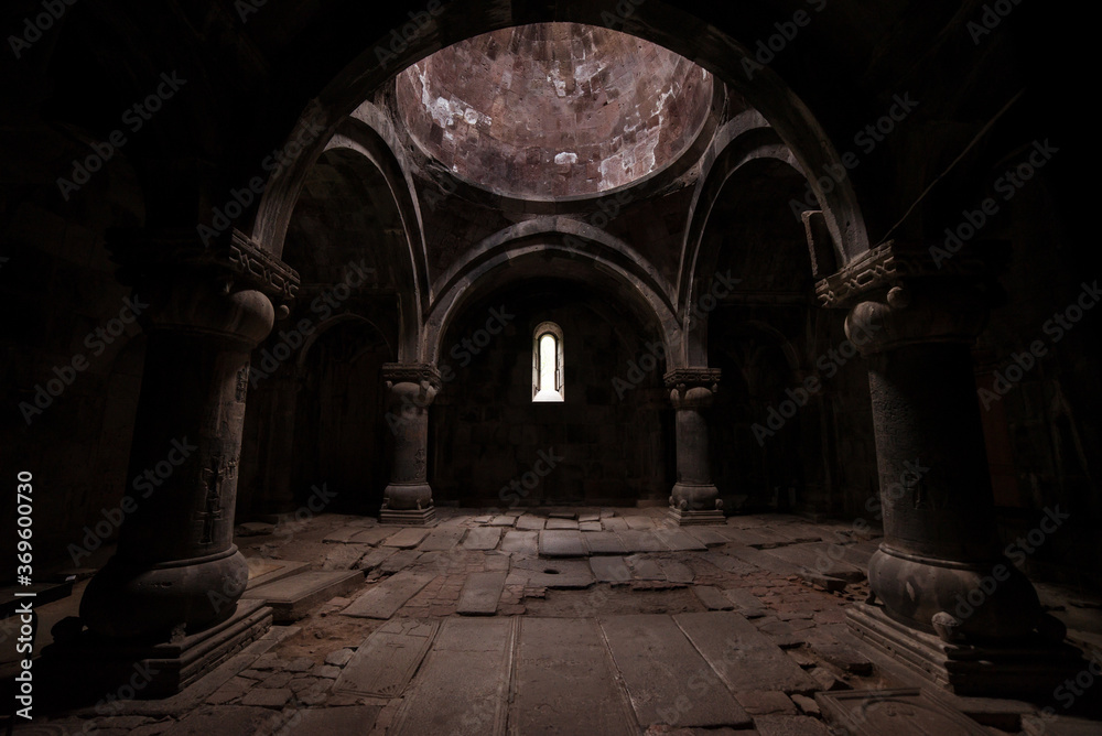 Interior of old Sanahin Armenian Monastery of the Armenian Apostolic Church with ray of light entering through narrow window and headstones on uneven ground