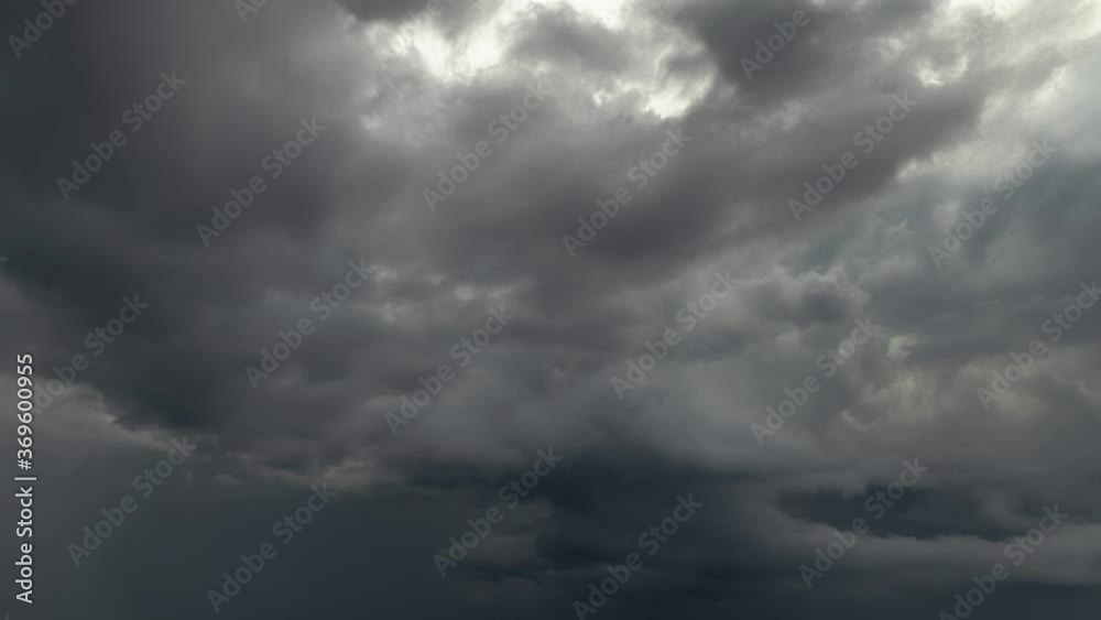 Feathery gray storm clouds churn and begin to dissipate in the overcast sky with sunlight lighting the upper clouds moving in different direction.