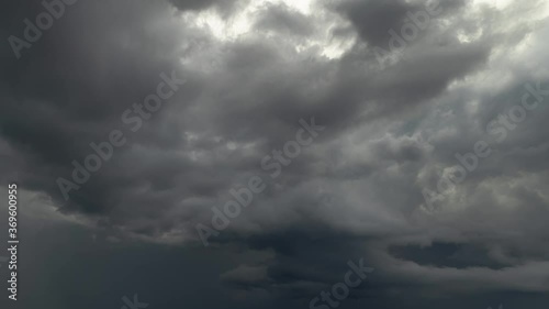Feathery gray storm clouds churn and begin to dissipate in the overcast sky with sunlight lighting the upper clouds moving in different direction.