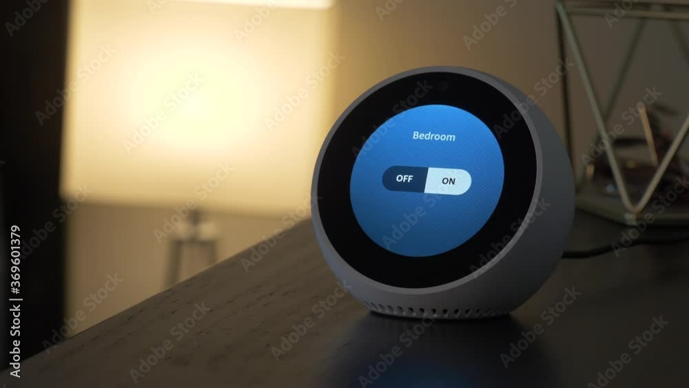 Smart speaker on the corner of a bedroom table switching a lamp ON using voice command