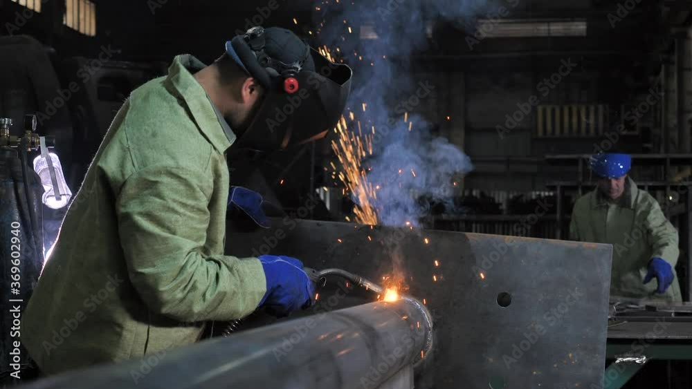 Industrial process, heat electrode work, metal parts welding with soldering iron by two men laborers team wearing safety uniform at heavy manufacturing factory indoor. Metalwork assembly, construction