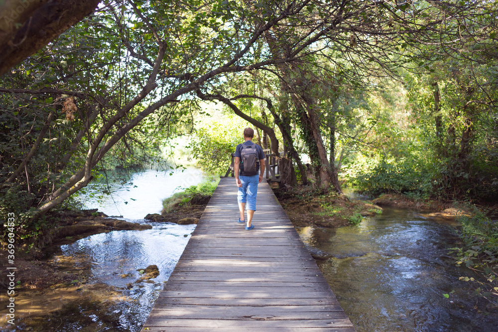 A man with a backpack goes on a wooden bridge.