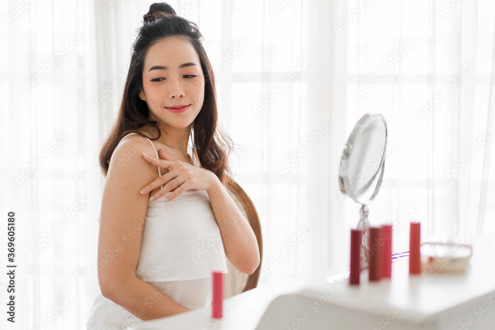 Smiling of young beautiful asian woman clean fresh healthy white skin looking at mirror.girl touching on her arm with hand and applying cream at home.spa and beauty concept Smiling of young beautiful asian woman clean fresh healthy white skin looking at mirror.girl touching on her arm with hand and applying cream at home.spa and beauty concept