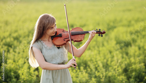 Romantic woman, girl with loose hair playing the violin. Sunset light in nature