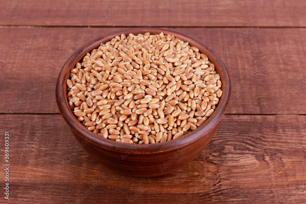 Wheat grains in ceramic bowl on brown wooden table. Top view, high angle, closeup. Harvest, healthy food, ingredient concept Wheat grains in ceramic bowl on brown wooden table. Top view, high angle, closeup. Harvest, healthy food, ingredient concept