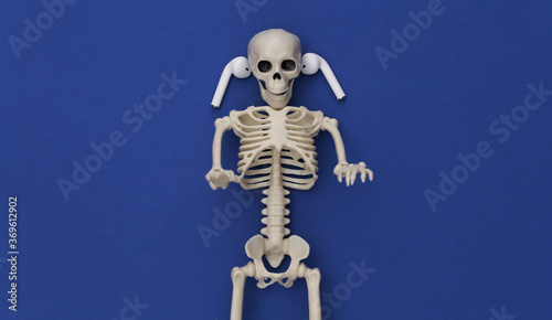 Skeleton and wireless headphones on classic blue background. Top view