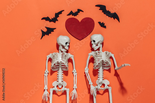 Two Skeletons, bats and red decorative heart on a bright orange background. Valentine's day or halloween theme. Top view. Flat lay