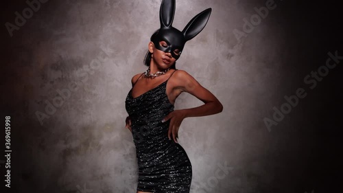 Portrait of beautiful flirting Asian woman in black dress and rabbit mask playfully dancing in the spotlight