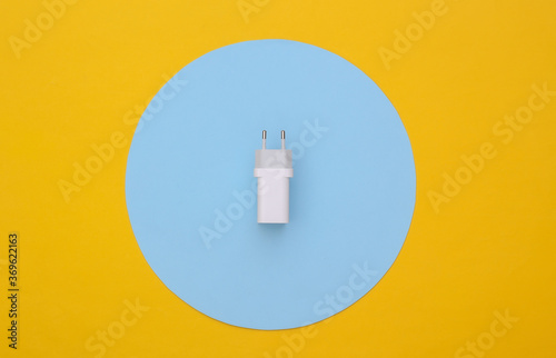 Charger adapter on yellow background with blue circle. Top view. Minimalism flat lay