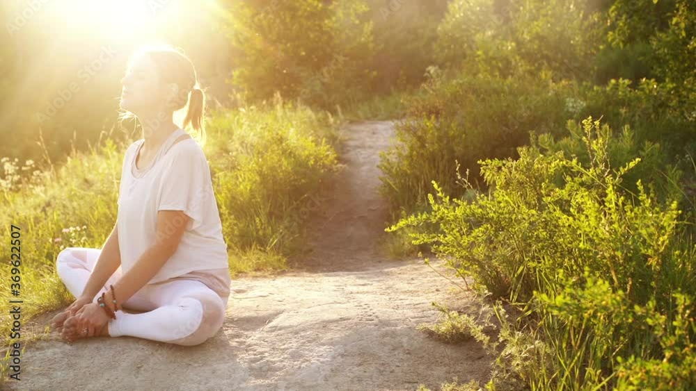 Calmly young yogini woman sitting Bound Angle Pose and raising head to sun outside in nature evening on background of bright sunray. Meditative girl practicing yoga exercises in alone outdoors sunset. Calmly young yogini woman sitting Bound Angle Pose and raising head to sun outside in nature evening on background of bright sunray. Meditative girl practicing yoga exercises in alone outdoors sunset.
