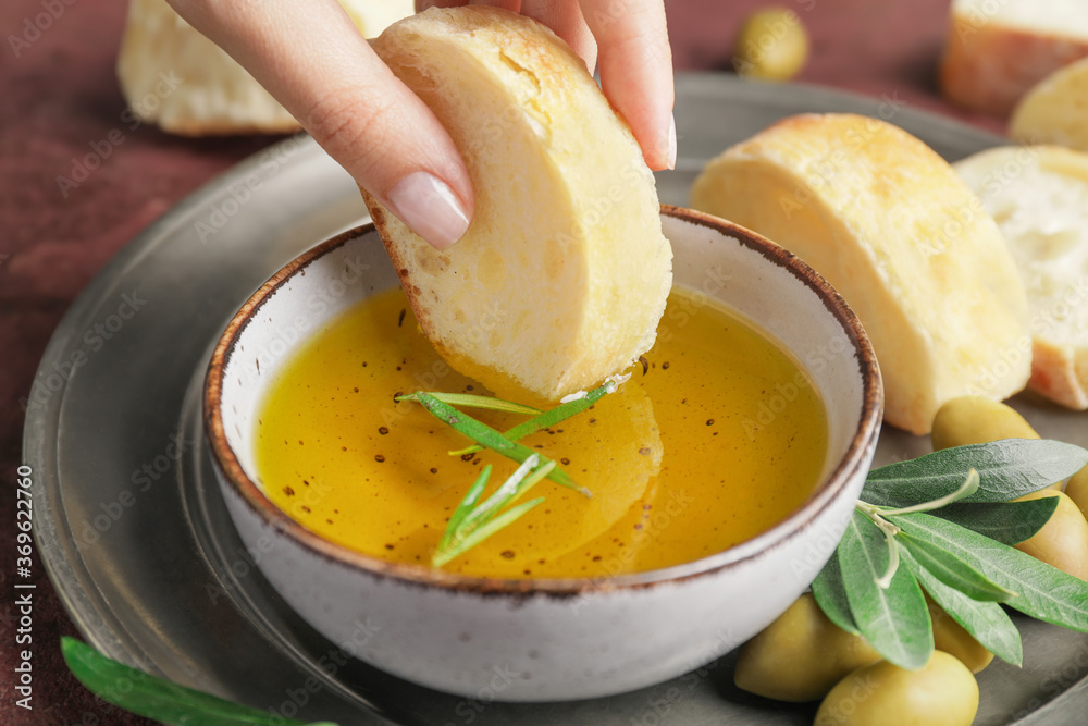 Woman dipping bread into bowl of tasty olive, closeup