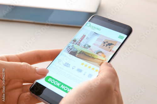 Woman with mobile phone booking room in hotel online, closeup