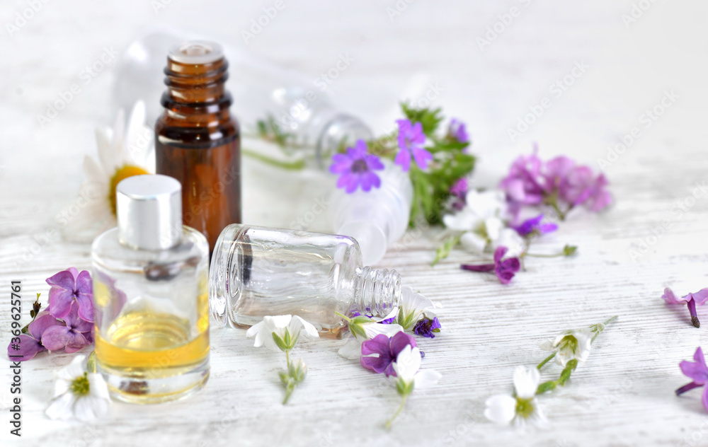 bottles of essential oil and colorful petals of flowers on white table