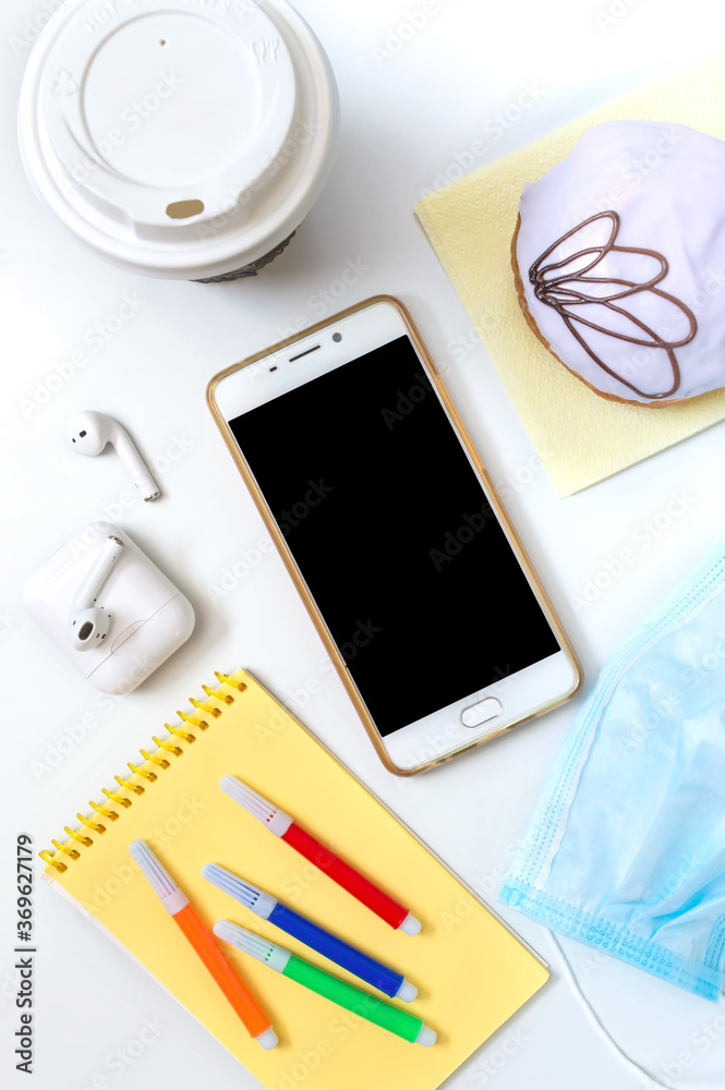 Mobile phone, donut, coffee, headphones, medical mask and materials for creativity on a white office desk. Snack dessert at the workplace, lunch break. Food ordering concept Mobile phone, donut, coffee, headphones, medical mask and materials for creativity on a white office desk. Snack dessert at the workplace, lunch break. Food ordering concept