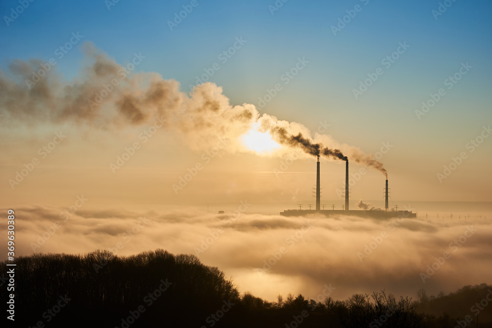 Horizontal snapshot of industrial area at setting sun, three smoking pipes from thermal power station pollute the atmosphere with black smog, concept of man-made disaster, environmental pollution