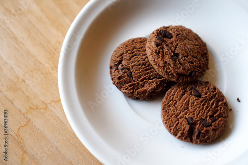 chocolate cookies and dark chocolate grain on white plate. snack theme on wooden table background