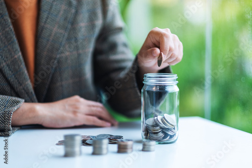 Closeup image of a businesswoman collecting and putting coins in a glass jar