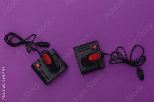 Two wired retro joysticks with wound cable on purple background. Video game, gaming. Top view